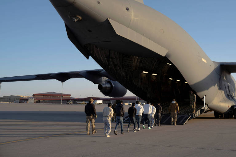 Pessoas fazem fila para entrar， algemadas， em um avião militar de carga com a porta traseira aberta