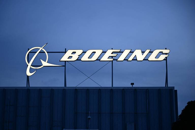 A imagem mostra o logotipo da Boeing iluminado em um fundo azul escuro. O logotipo é composto pelo nome 039;BOEING039; em letras grandes e brancas， com um símbolo de um avião estilizado à esquerda.