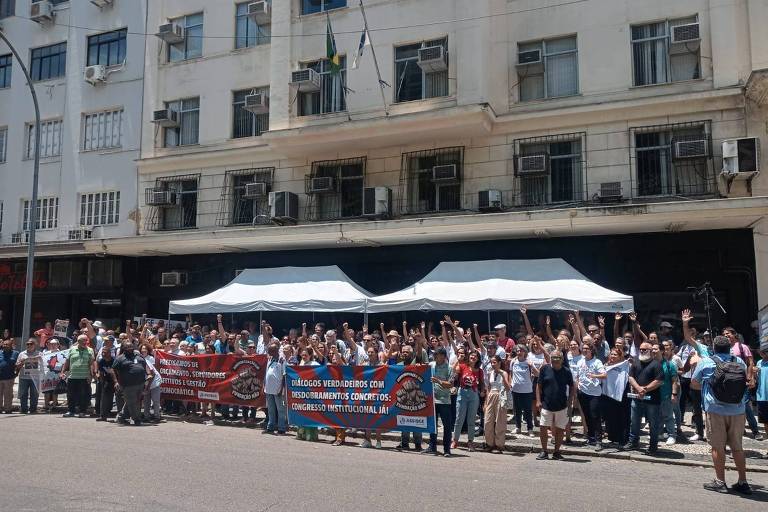 Imagem mostra protesto de servidores do IBGE contra a gestão do presidente Marcio Pochmann no Rio de Janeiro. Eles estão com os braços levantados e seguram faixas. 