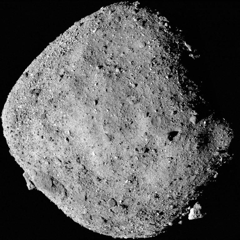 O asteroide Bennu Imagem do asteroide Bennu， mostrando sua forma irregular e superfície repleta de crateras e rochas. O fundo é negro， destacando o asteroide.
