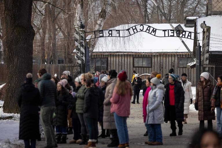 A imagem mostra um grupo de pessoas em uma fila， em um ambiente ao ar livre com neve no chão. As pessoas estão vestidas com roupas de inverno， algumas usando gorros e cachecóis， e parecem estar aguardando para entrar no local