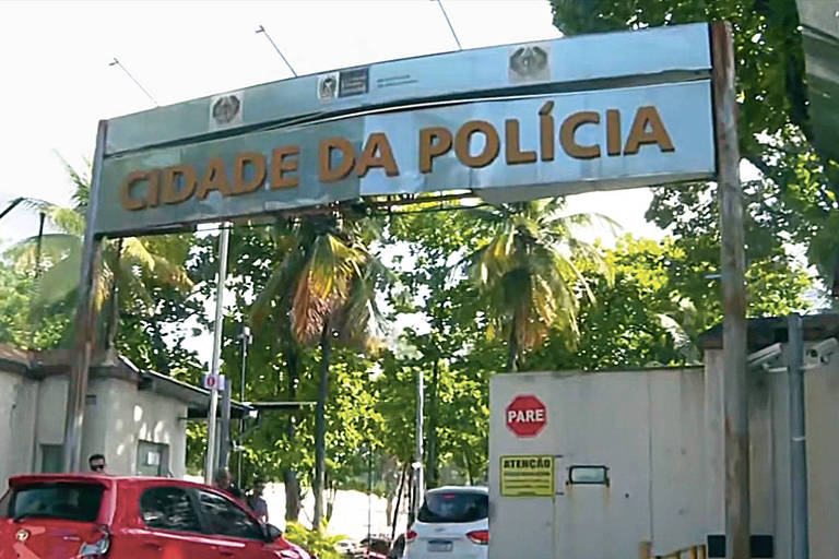 A imagem mostra a entrada de uma delegacia de polícia， com um grande letreiro em cima que diz 039;CISDAS DA POLÍCIA039;. Ao fundo， há árvores e um ambiente urbano. Dois carros estão estacionados na frente， um vermelho e um branco.