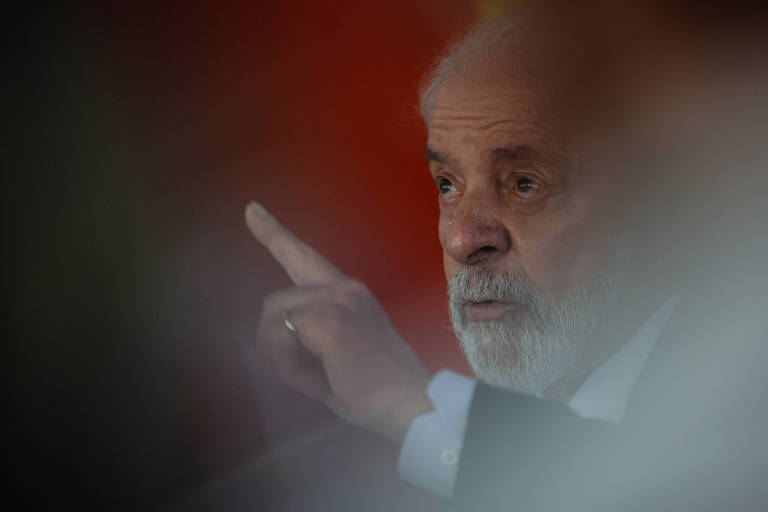 A imagem mostra um homem com cabelo grisalho e barba, gesticulando com a mão direita enquanto fala. O fundo é desfocado, mas parece ter uma cor sólida. O homem parece estar em um ambiente de discurso ou apresentação.
