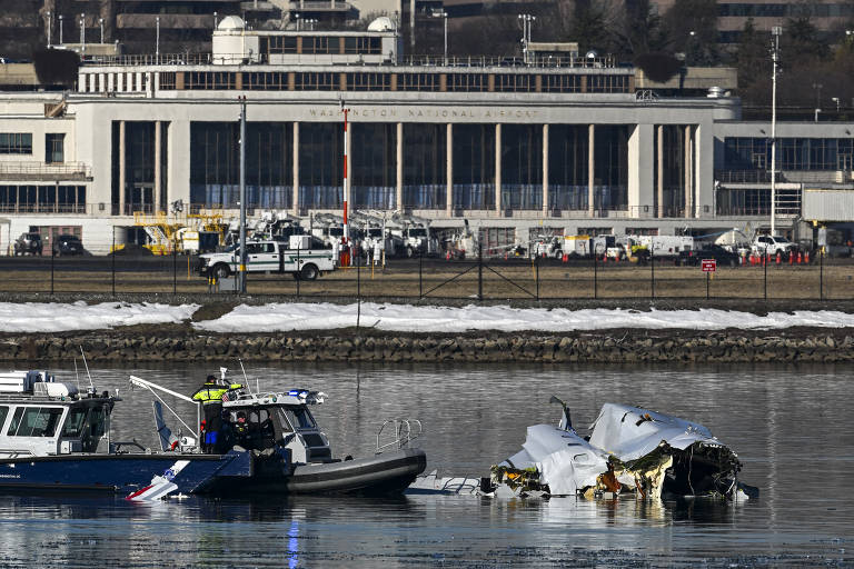 A imagem mostra um barco de resgate próximo a destroços de uma aeronave submersa em água, com um aeroporto ao fundo. O aeroporto possui uma arquitetura moderna e é cercado por veículos de serviço. A cena é iluminada por luz natural, e há neve visível na margem.