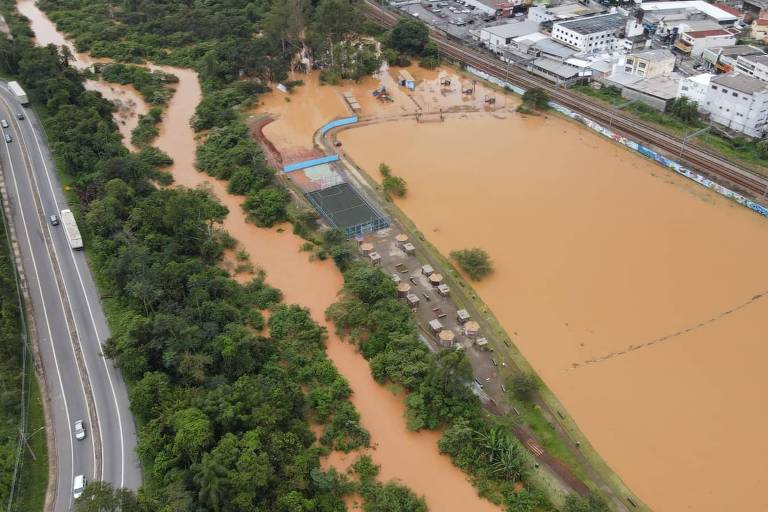 Local alagado com água cor de laranja visto de cima ao lado de uma rodovia e de um bairro de casas