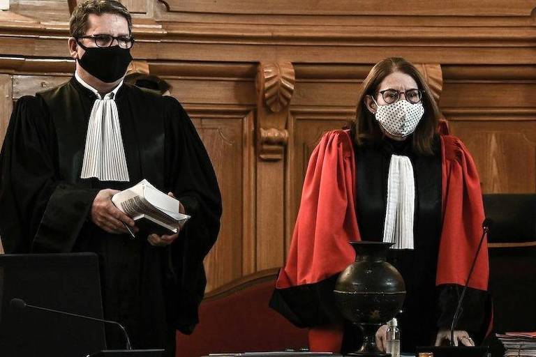 Dois juízes em um tribunal， ambos usando máscaras. O juiz à esquerda está segurando um livro e vestindo uma toga preta com uma gravata branca. A juíza à direita está usando uma toga vermelha e uma máscara branca com padrões. O ambiente é de um tribunal， com painéis de madeira ao fundo.