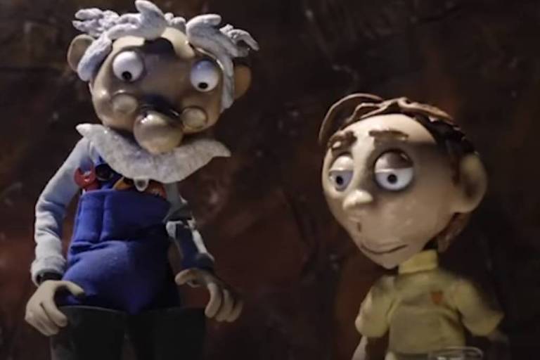 A imagem mostra dois personagens de animação em stop motion. O primeiro personagem, um idoso com cabelo grisalho e óculos, usa um macacão azul e uma camisa branca. Ele tem um bigode e uma expressão facial curiosa. O segundo personagem é um jovem com cabelo castanho claro, usando uma camisa amarela. Ambos estão em um ambiente com fundo escuro e texturizado.