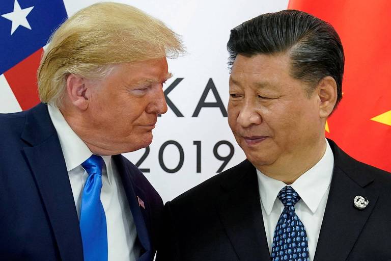 A imagem mostra dois homens em um encontro， um deles com cabelo loiro e terno escuro， e o outro com cabelo escuro e terno claro. Ao fundo， estão as bandeiras dos Estados Unidos e da China. Os homens parecem estar em uma conversa próxima.