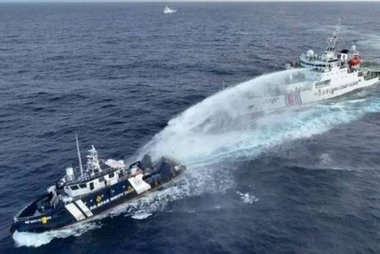 A imagem mostra dois navios no mar. Um dos navios， de cor escura， está em primeiro plano e parece estar lançando água， enquanto o outro， de cor clara， está mais ao fundo. O mar está calmo， e há uma pequena embarcação visível ao fundo. No canto superior direito， há um texto que diz 039;Courtesy of NTF-WPS039;.