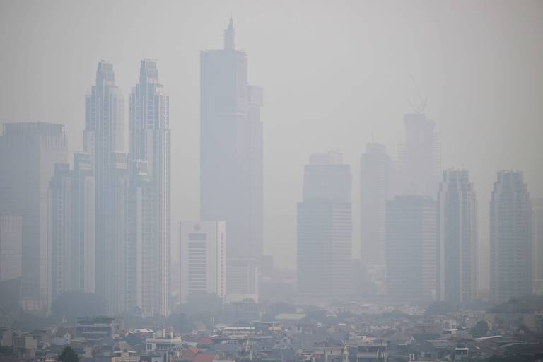 A imagem mostra um horizonte urbano coberto por uma densa neblina， com vários arranha-céus visíveis. Os edifícios têm formas variadas e estão parcialmente ocultos pela poluição do ar， criando uma atmosfera de baixa visibilidade.