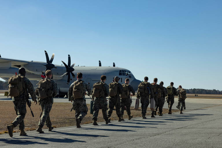 Um grupo de soldados caminha em direção a uma aeronave militar， um avião de transporte， estacionado em uma pista. Os soldados estão vestidos com uniformes camuflados e carregam mochilas. O céu está claro e o ambiente é de um campo de aviação.