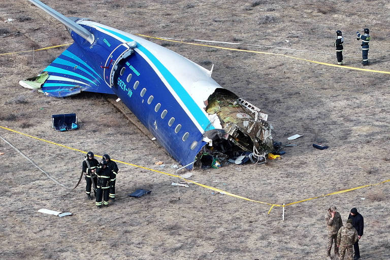 Vista aérea de local de acidente mostra resto da cauda de um avião pintado em tons de azul， com investigadores em volta