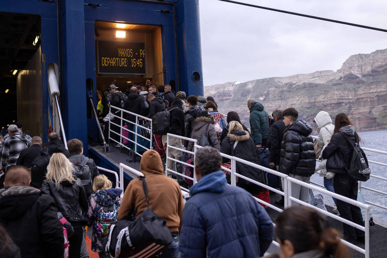 A imagem mostra um grupo de pessoas em fila para embarcar em um ferry. As pessoas estão subindo uma escada que leva à entrada do barco， com algumas usando casacos e mochilas. Ao fundo， é possível ver uma paisagem montanhosa e o mar