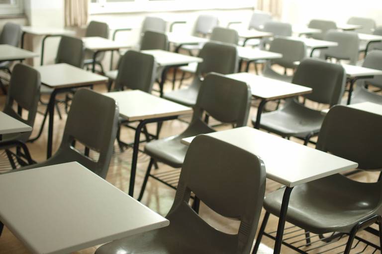 A imagem mostra uma sala de aula com mesas vazias