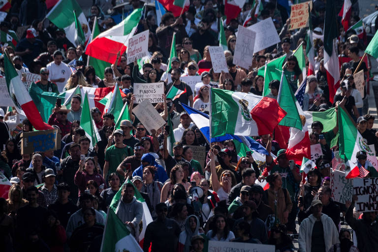 A imagem mostra uma grande multidão em uma manifestação， segurando bandeiras do México. As bandeiras são predominantemente verdes， brancas e vermelhas. Há também cartazes visíveis， mas o texto neles não é legível. A cena é vibrante e cheia de pessoas， refletindo um forte sentimento de união e protesto