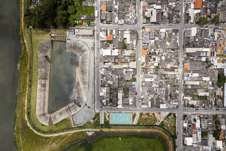 Imagem aérea de uma área urbana， mostrando um conjunto de ruas e edifícios. À esquerda， há uma estrutura retangular que parece ser um reservatório ou piscina， e à direita， uma área com várias casas e prédios. O espaço é delimitado por um corpo d039;água na parte inferior da imagem.