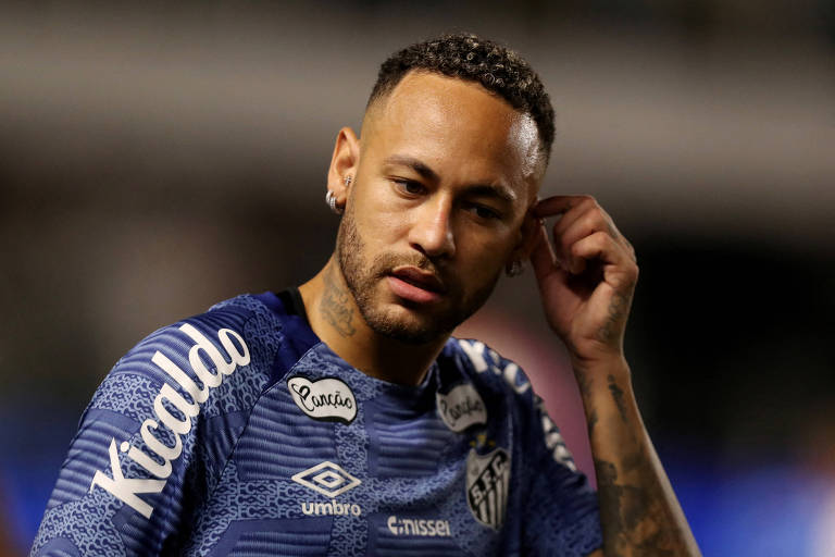 A imagem mostra o jogador Neymar com a mão da orelha esquerda. Ele veste uma camisa do Santos