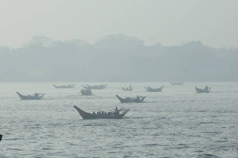 A imagem mostra vários barcos flutuando em uma água calma， com uma névoa densa cobrindo a cena. O fundo é indistinto devido à neblina， mas sugere uma paisagem natural com árvores ou colinas. Os barcos estão dispersos， alguns mais próximos e outros mais distantes.