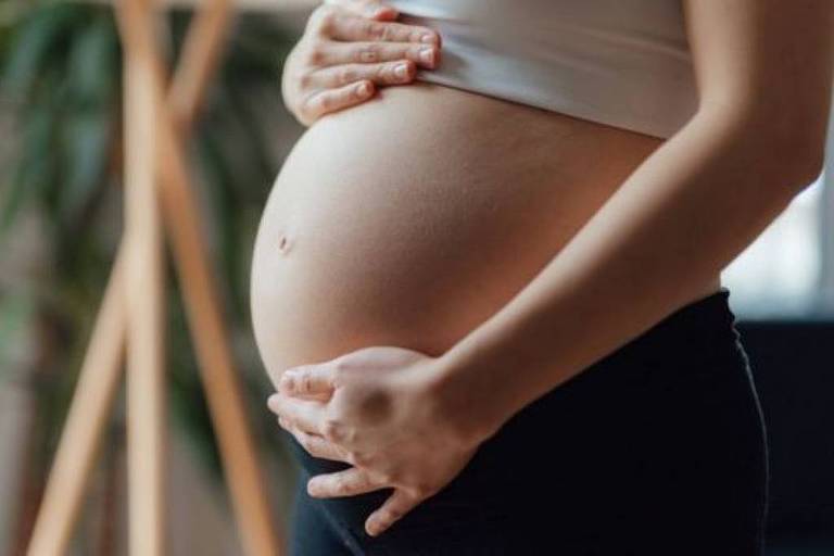 Mulher branca gravida passando as mãos pela barriga