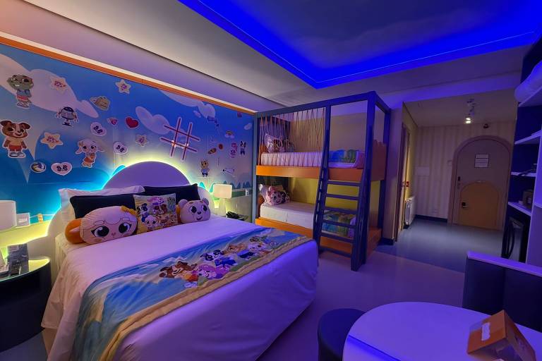 O quarto apresenta uma decoração temática com uma cama de casal à esquerda, coberta por um edredom colorido. Ao fundo, há uma parede decorada com nuvens e personagens infantis. À direita, uma beliche com escada e prateleiras coloridas. O ambiente é iluminado por luzes azuis no teto, criando uma atmosfera lúdica. Um pequeno sofá redondo e uma mesa estão visíveis na parte inferior da imagem.