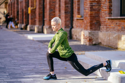 Middle age blond slim woman jogger in green activewear in an outdoor everyday sports routine. Female jogger workout, doing warming up exercise for legs. 
( Foto: Iryna / adobe stock ) DIREITOS RESERVADOS. NÃO PUBLICAR SEM AUTORIZAÇÃO DO DETENTOR DOS DIREITOS AUTORAIS E DE IMAGEM