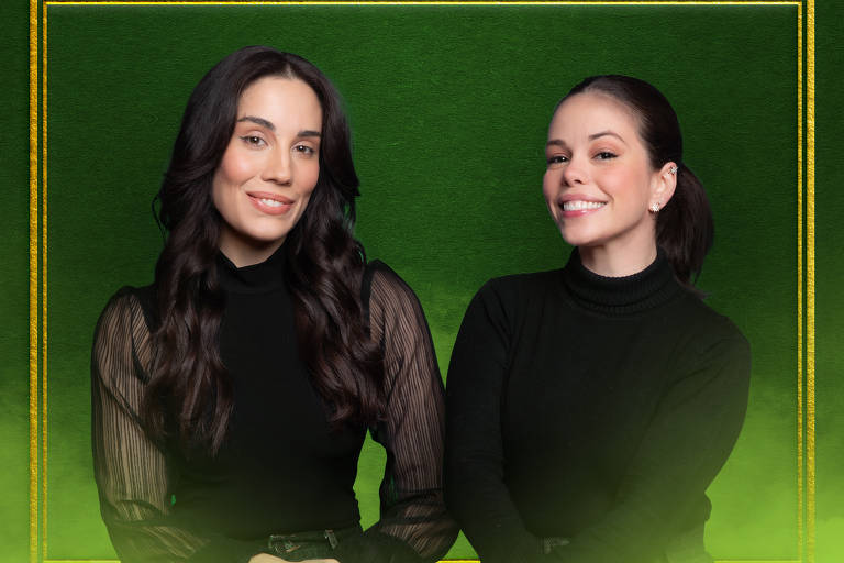 A imagem mostra duas mulheres sorrindo, sentadas lado a lado. Ambas estão vestidas de preto, com uma mulher à esquerda usando uma blusa de mangas longas e a outra à direita usando um suéter de gola alta. O fundo é verde com uma moldura dourada, criando um contraste vibrante.