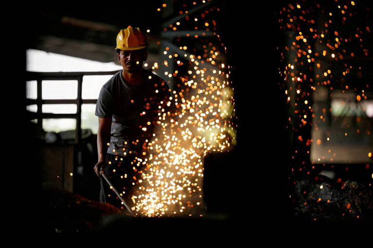 Um trabalhador está em um ambiente industrial， usando um capacete amarelo e operando uma máquina que gera faíscas. O fundo é escuro， destacando as faíscas brilhantes que estão sendo emitidas durante o trabalho.