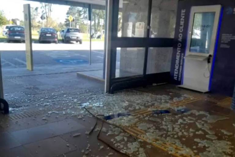 Porta com transparente quebrado e estilhaços de vidro espalhados pelo chão na entrada do aeroporto 