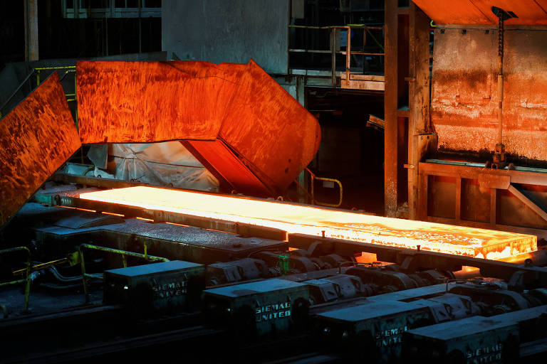 A imagem mostra um ambiente industrial onde uma longa peça de metal quente está sendo processada. O metal é de cor laranja brilhante， indicando alta temperatura， e está sendo transportado em uma linha de produção. Ao fundo， há uma estrutura metálica e equipamentos industriais， com iluminação que destaca o brilho do metal.
