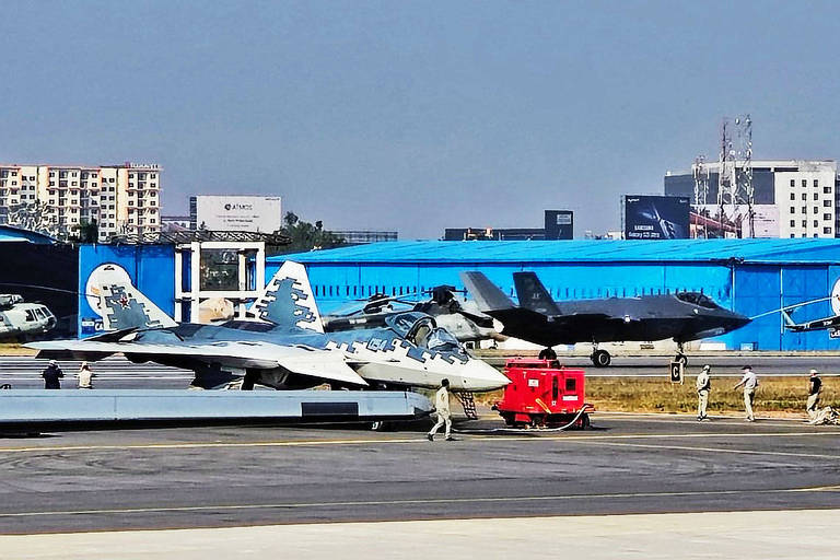 Avião cinza escuro passa por trás de outro， branco e azul