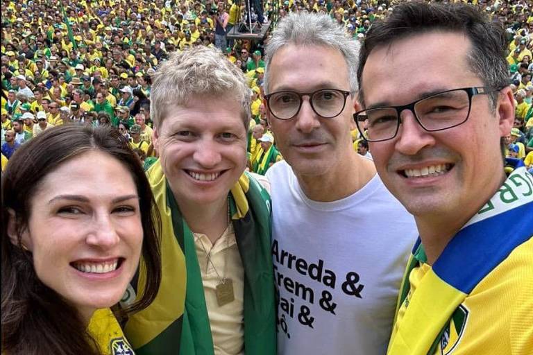 Os quatro sorriem em selfie e estão em caminhão de som acima de multidão que veste verde e amarelo