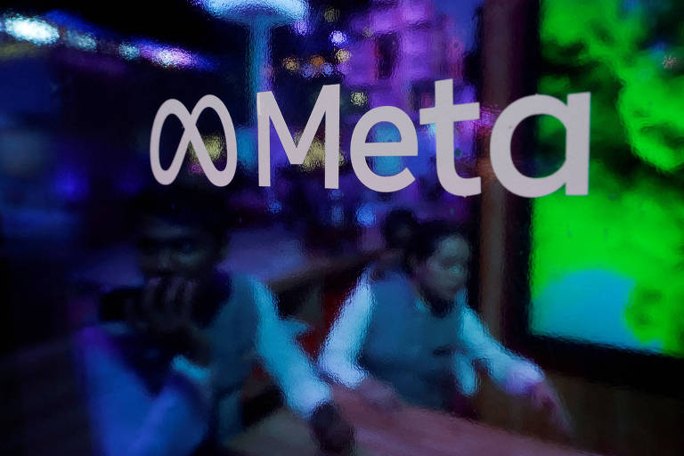 A imagem mostra o logotipo da Meta em destaque， com um fundo colorido e desfocado. Duas pessoas estão visíveis em primeiro plano， uma delas segurando um celular e a outra sentada à mesa. O ambiente é iluminado com luzes em tons de roxo e verde.
