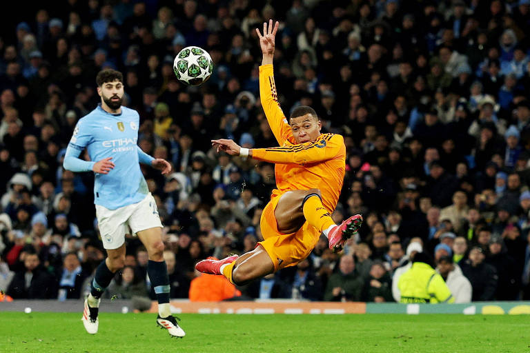 Um jogador de futebol vestido com um uniforme laranja está saltando para defender a bola， enquanto um jogador adversário， vestido com um uniforme azul claro， observa a jogada. O fundo mostra uma multidão em um estádio， com luzes e um clima de competição.
