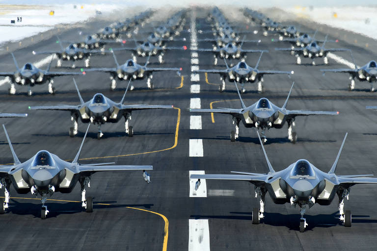 Diversos aviões de caça cinzentos alinhados em uma pista de pouso