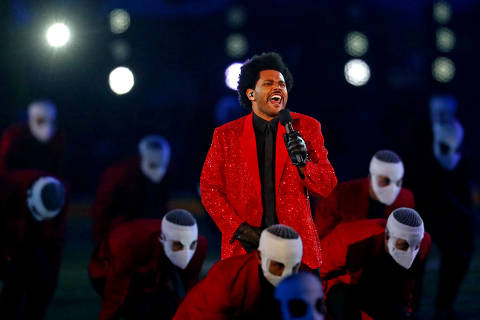 O cantor se apresentou no intervalo do Super Bowl em 2021, que teve capacidade de público limitada devido à pandemia de Covid-19 *** Local Caption *** Um artista em um paletó vermelho brilhante canta em um palco, cercado por dançarinos que usam roupas vermelhas e máscaras brancas. O artista está segurando um microfone e parece estar se apresentando com energia, enquanto os dançarinos se inclinam em sua direção. O fundo é iluminado com luzes brilhantes. ORG XMIT: AGEN2102072255869263