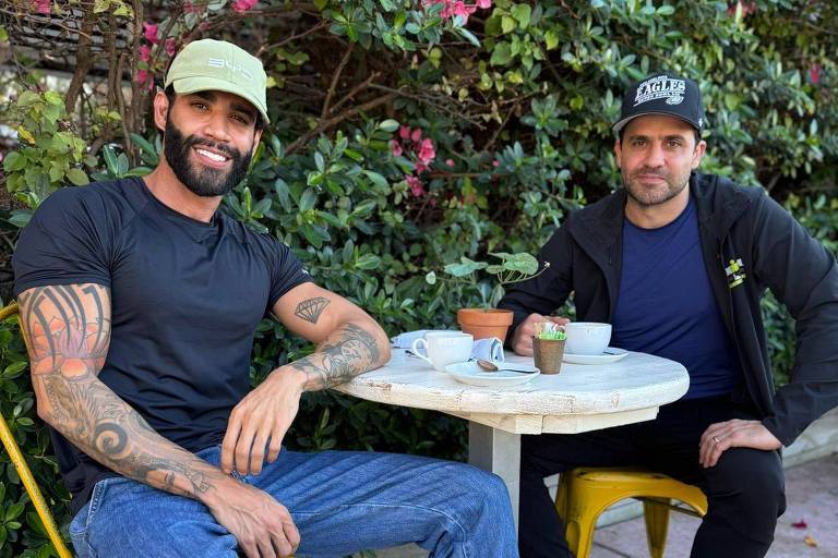 Os dois estão sentados em um jardim， usam boné e sorriem para a câmera