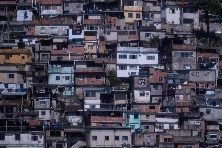 A imagem mostra uma densa aglomeração de casas em uma comunidade urbana. As construções são de diferentes tamanhos e cores， com predominância de tons terrosos e algumas casas pintadas em azul e amarelo. As casas estão empilhadas umas sobre as outras， formando uma paisagem vertical. Algumas janelas estão abertas e há varandas visíveis.