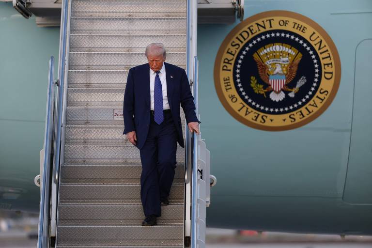 De terno escuro e gravata， Donald Trump desce as escadas de um avião. Ao fundo， é visível o emblema do presidente dos Estados Unidos， que inclui uma águia e a frase 039;SEAL OF THE PRESIDENT OF THE UNITED STATES039;.