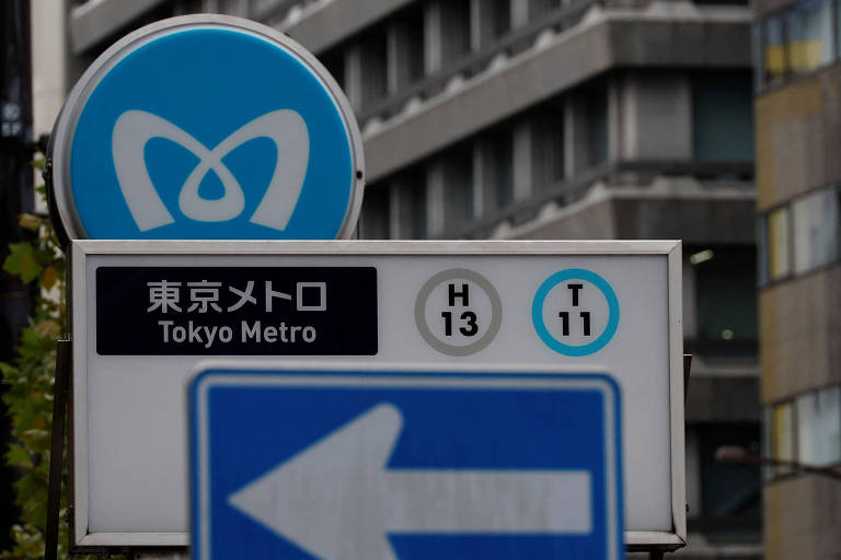 A imagem mostra um sinal de direção para o Metrô de Tóquio. O sinal inclui o logotipo do metrô em azul， além de texto em japonês e inglês que diz 039;東京メトロ039; e 039;Tokyo Metro039;. Também estão presentes os números H 13 e T 11， indicando linhas do metrô， e uma placa de direção com uma seta apontando para a esquerda.