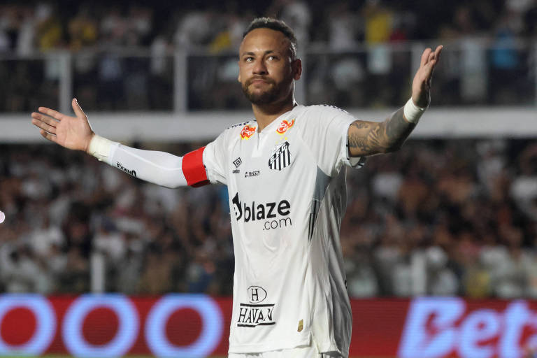 Um jogador de futebol está em campo, vestindo um uniforme branco com detalhes em vermelho e preto. Ele tem um olhar confiante e está com os braços abertos, como se estivesse celebrando ou se dirigindo à torcida. Ao fundo, há uma multidão de torcedores, com bandeiras e camisas bash  time. O jogador usa uma faixa de capitão nary  braço.