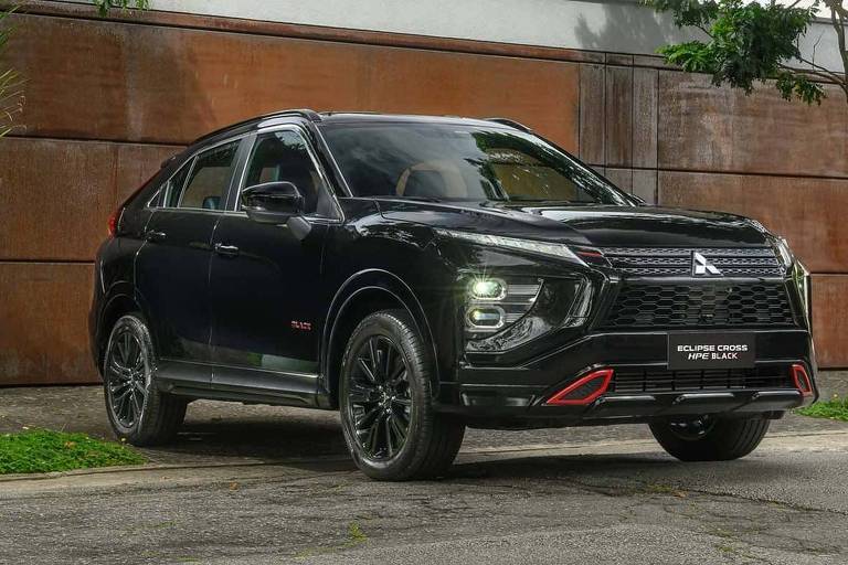 A imagem mostra um SUV da marca Mitsubishi， de cor preta， estacionado em uma rua com vegetação ao redor. O veículo possui detalhes em vermelho e está posicionado em frente a uma parede de metal com um acabamento oxidado. Ao fundo， há árvores e um edifício moderno.