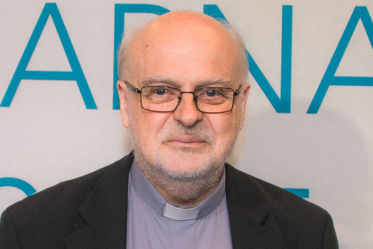 Um homem idoso com cabelo grisalho e calvo, usando óculos e uma camisa de colarinho claro. Ele está vestido com um paletó escuro e uma batina. O fundo é claro com texto em azul que diz 'HABITAR O MUNDO'.