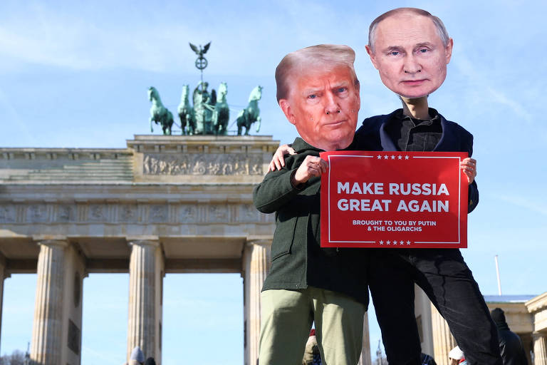 A imagem mostra duas pessoas em frente ao Portão de Brandemburgo， em Berlim. Uma delas está vestindo uma máscara com o rosto de Donald Trump e a outra com o rosto de Vladimir Putin. Ambas seguram um cartaz vermelho que diz 039;MAKE RUSSIA GREAT AGAIN039;. O céu está claro e o monumento é visível ao fundo.