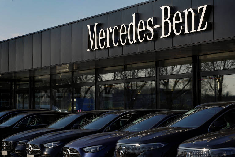 A imagem mostra uma concessionária da Mercedes-Benz， com o nome da marca em destaque na parte superior. Na frente， há uma fila de carros pretos da marca， estacionados em frente ao edifício. O ambiente parece ser ao ar livre， com janelas grandes ao fundo.