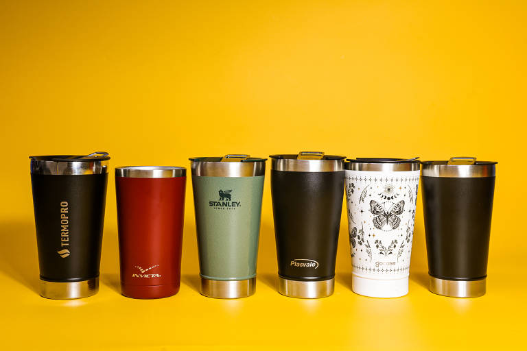 A imagem apresenta seis canecas de diferentes cores e designs dispostas em uma superfície amarela. As canecas variam em tonalidades, incluindo preto, vermelho, verde e uma com um padrão de animais. Cada caneca possui uma tampa e detalhes em aço inoxidável.