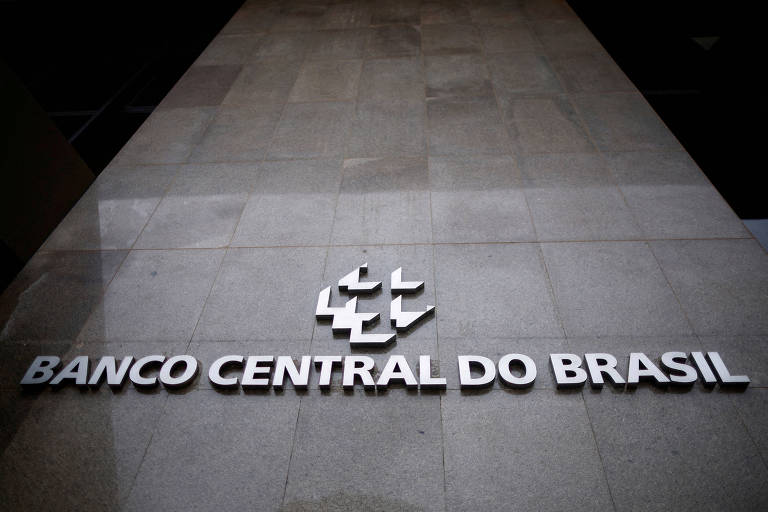 A imagem mostra a fachada do Banco Central do Brasil， com o nome 039;BANCO CENTRAL DO BRASIL039; em letras grandes e em destaque. O fundo é de pedra clara， e o logotipo do banco está acima do nome.