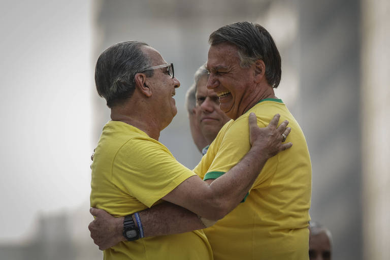 O ex-presidente Jair Bolsonaro e o pastou Silas Malafaia se abraçam em um evento público， vestindo camisetas amarelas. Ambos estão sorrindo e demonstrando alegria. Ao fundo， o governador Tarcísio de Freitas está com expressão neutra. O ambiente parece ser ao ar livre， com edifícios desfocados ao fundo.