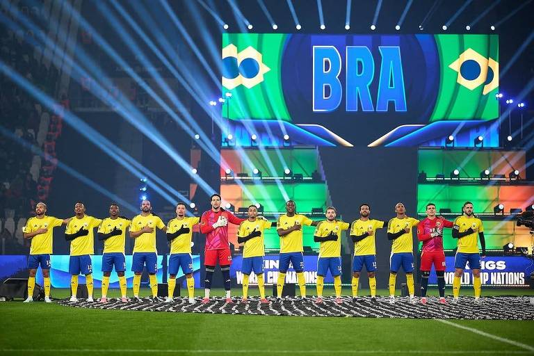 A imagem mostra a equipe de futebol do Brasil em uma cerimônia de apresentação. Os jogadores estão alinhados em uma formação， usando uniformes amarelos com detalhes azuis. O goleiro， que está à frente， veste um uniforme vermelho. Ao fundo， há uma tela grande exibindo a palavra 039;BRA039; e elementos gráficos que representam o Brasil， com luzes e efeitos visuais.