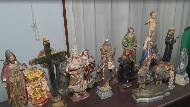 A imagem mostra uma coleção de estatuetas religiosas dispostas sobre uma superfície. As estatuetas incluem figuras de santos， uma cruz， e uma variedade de personagens， algumas delas vestidas com roupas tradicionais. As estatuetas são de diferentes tamanhos e estilos， com detalhes visíveis em suas vestimentas e expressões.