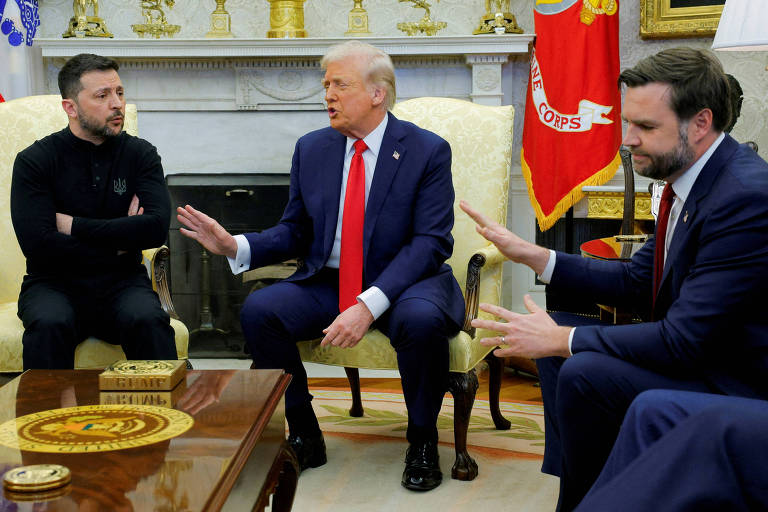 A imagem mostra uma reunião no Salão Oval da Casa Branca. Três homens estão sentados em um sofá. Um deles está vestido com uma camiseta preta e calças escuras， enquanto outro usa um terno azul escuro e uma gravata. O terceiro homem está vestido com um terno e gravata vermelha. Eles parecem estar em uma conversa， com gestos de mão. Ao fundo， há uma bandeira e uma decoração típica do ambiente.